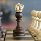 Dark wooden chess king with golden crown on chessboard, surrounded by blurred pieces
