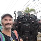 Smiling man with patterned shirt next to life-size black robot at outdoor event