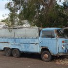 Vintage Blue Camper Van with Pop-Top Roof Parked Near Green Garbage Bin
