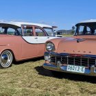 Vintage Rust-Colored Cars Parked on Grassy Field Under Clear Blue Sky