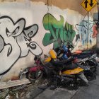 Weathered scooter against graffiti-covered wall on street with debris and foliage