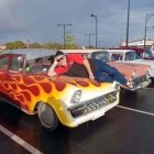 Custom-painted hot rod cars on mountain road with waving people