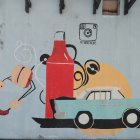Colorful street art mural with classic car and figure in red dress on grey wall