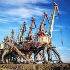 Giant bucket-wheel excavator in mining operation with cranes under clear blue sky