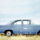 Vintage Blue Car Parked on Grass with Person by Open Trunk
