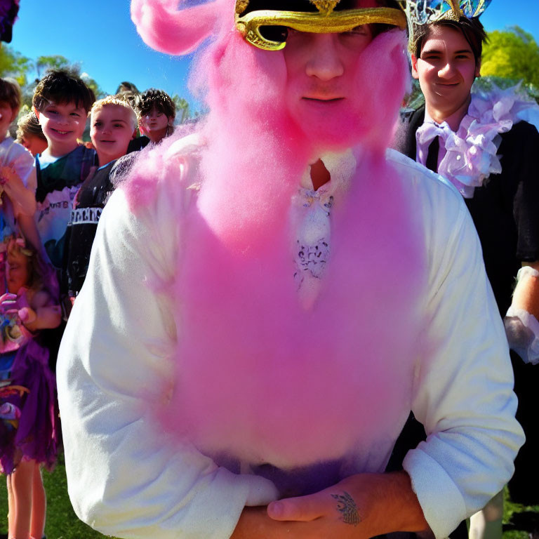 Children in costumes surround person in pink fluffy outfit with masquerade mask on sunny day