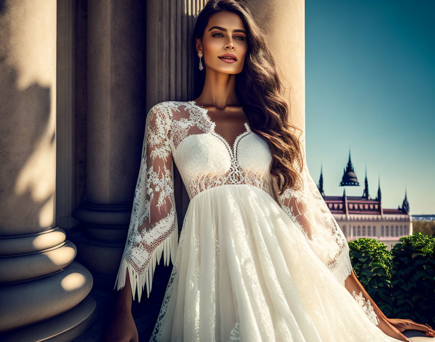 Woman in white lace gown by stone pillars and ornate building.