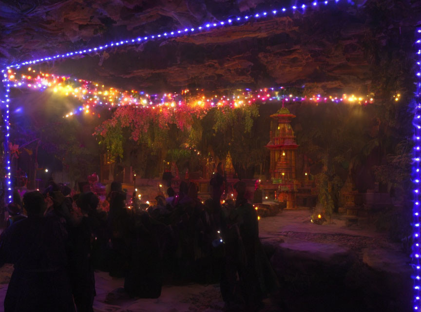 Nighttime gathering at illuminated shrine under rocky overhang