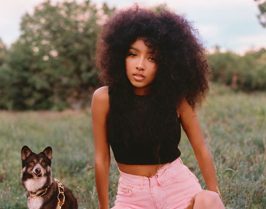 Curly-haired woman in crop top and pink shorts with dog in field