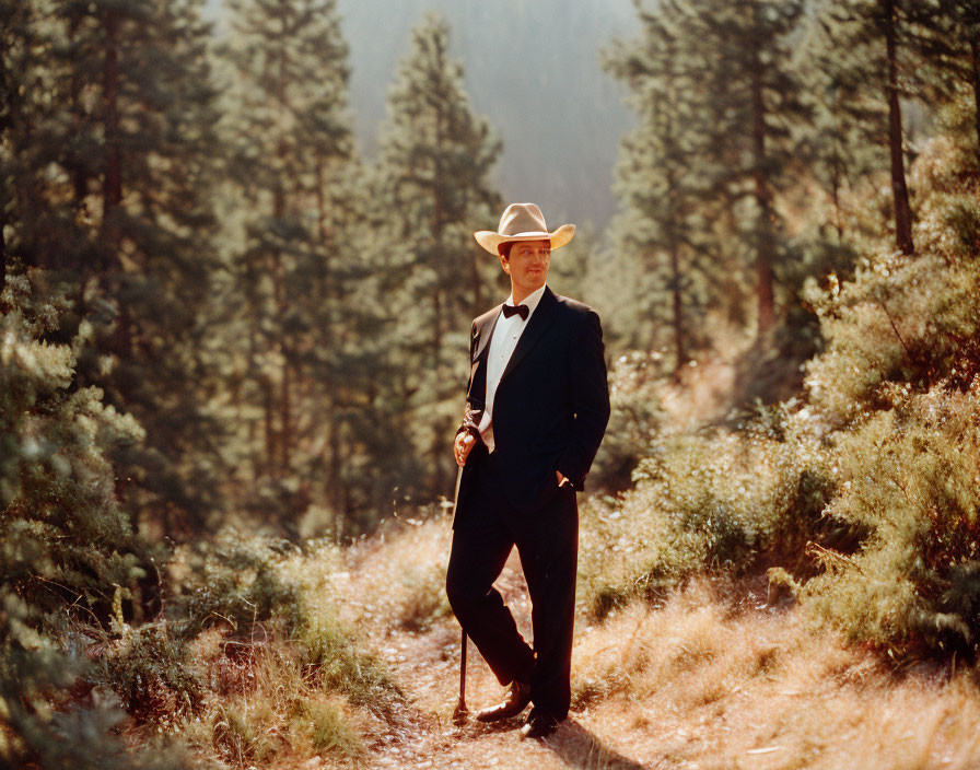 Person in tuxedo and cowboy hat on forest trail with greenery