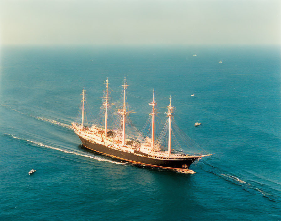 Tall ship with multiple masts sailing on calm sea with smaller boats