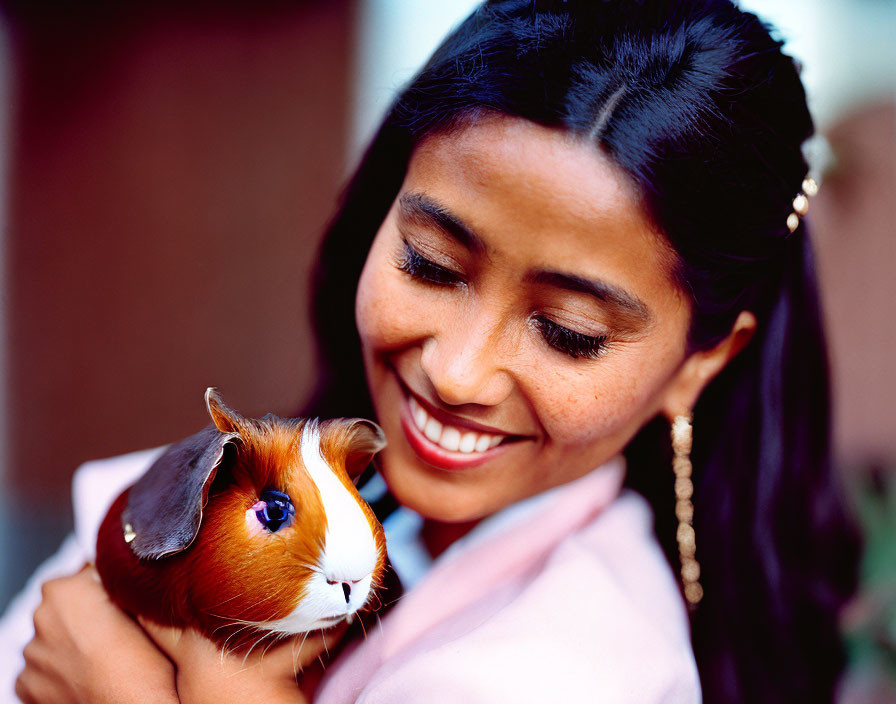 Smiling woman with long black hair holding guinea pig in pink outfit