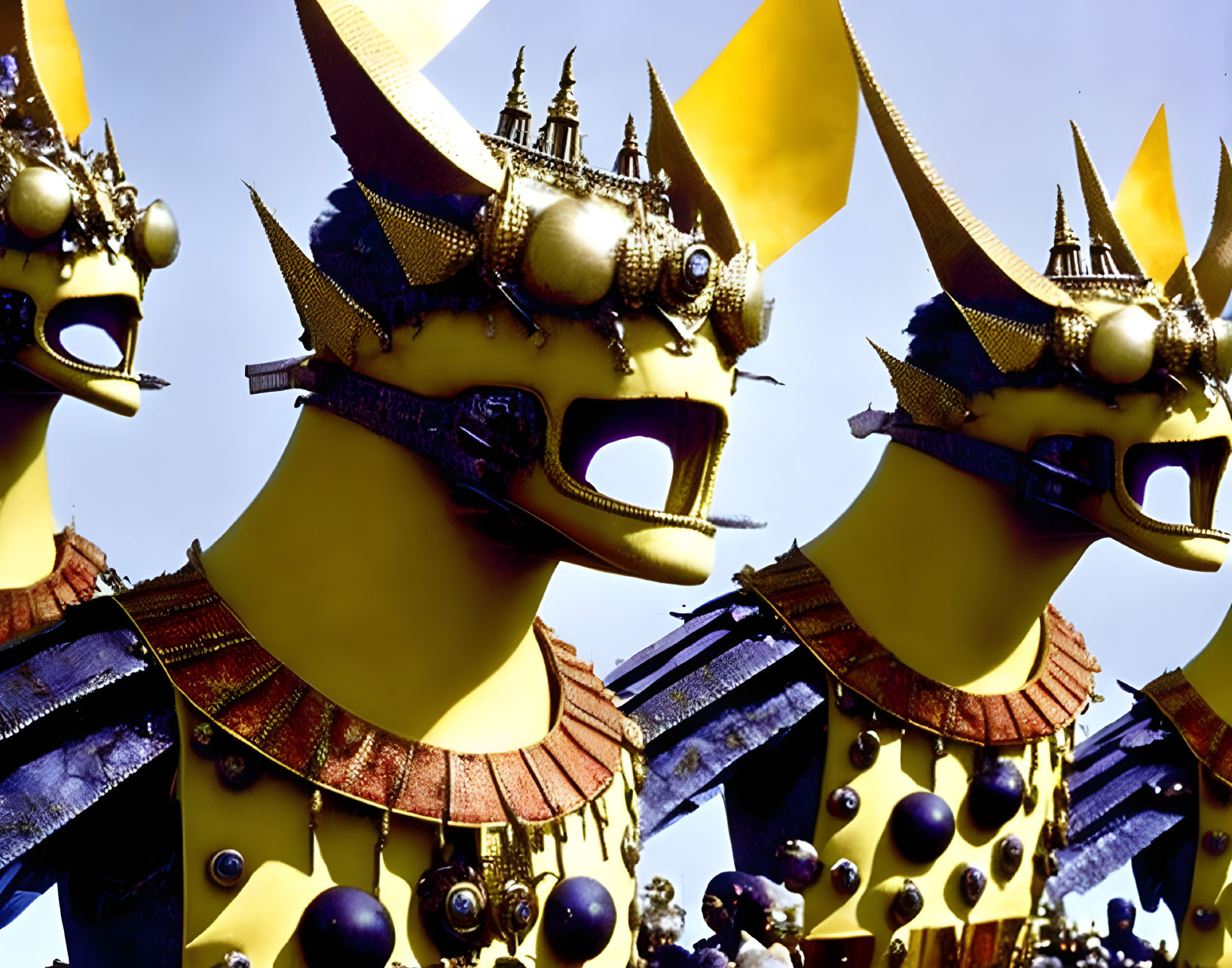 Elaborate golden masks on three figures against clear sky