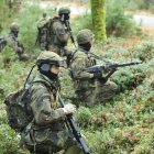 Military soldiers in camouflage gear navigating dense forest with rifles.