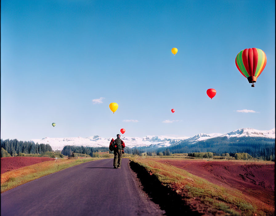Person walking on rural road with hot air balloons over scenic landscape