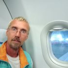 Gray-haired man gazes out airplane window at clouds