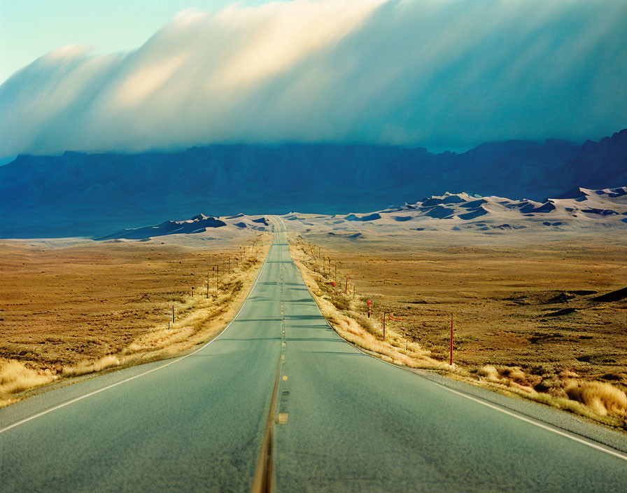 Straight Road Through Arid Landscape with Rolling Hills and Dramatic Clouds