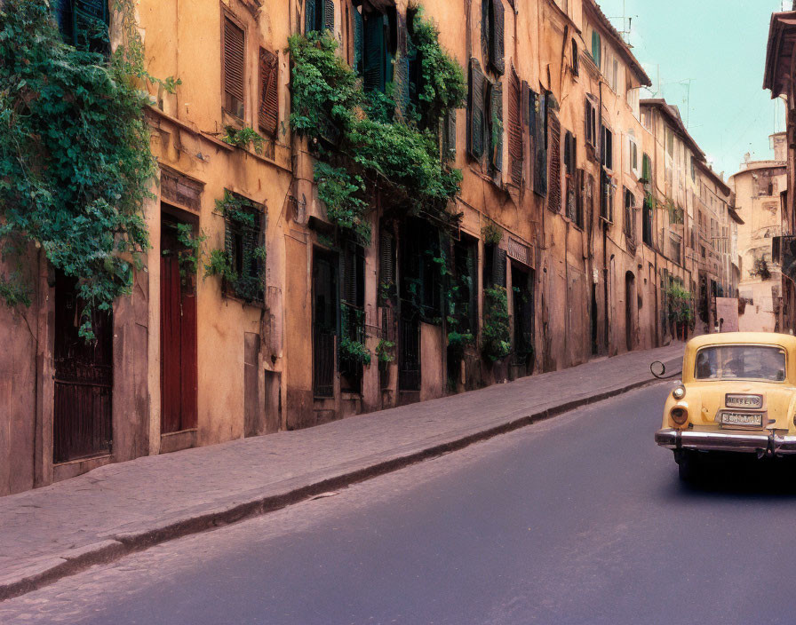 Vintage Yellow Car Driving on Narrow Cobblestone Street flanked by Weathered Terracotta Buildings