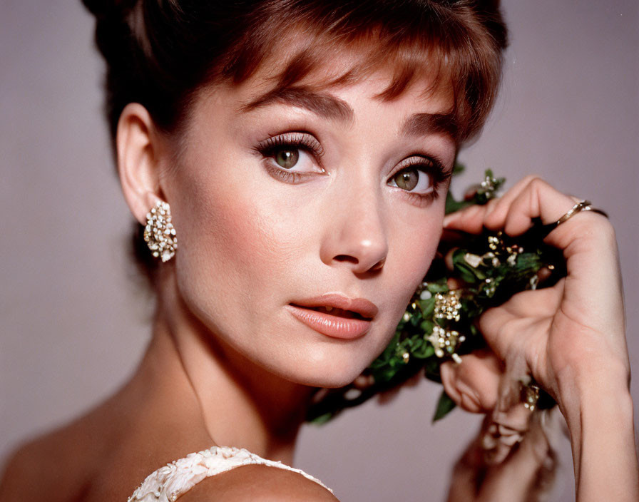 Woman portrait with classic hairstyle, sparkling earrings, holding greenery, captivating gaze
