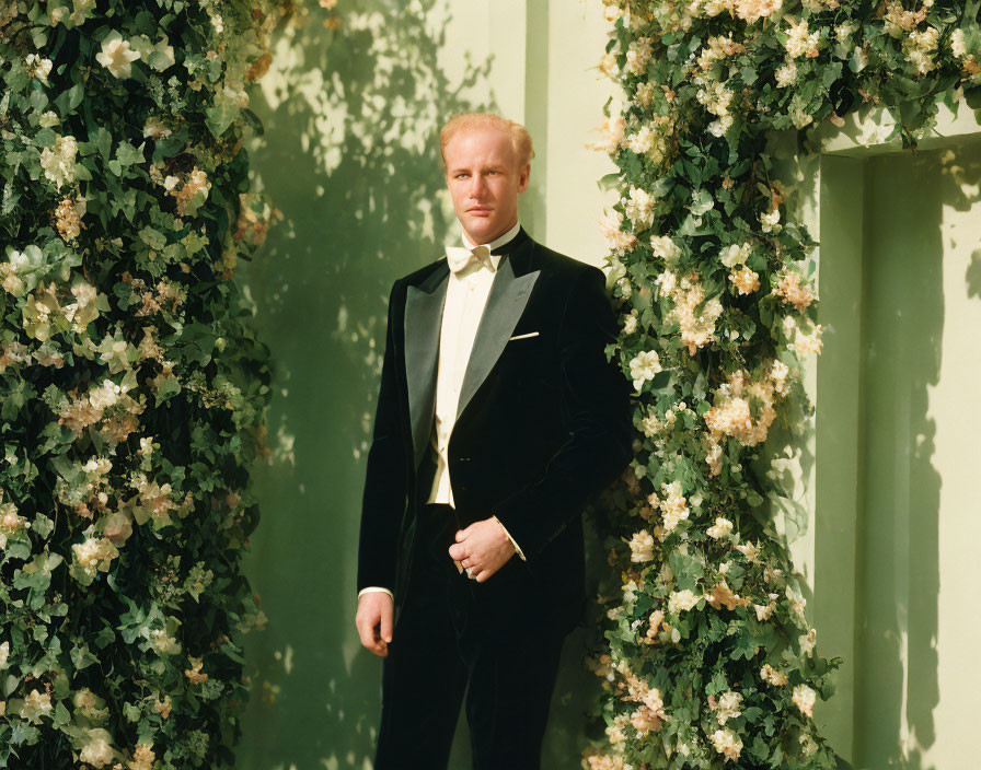 Man in Black Tuxedo Standing in Front of Green Foliage Wall