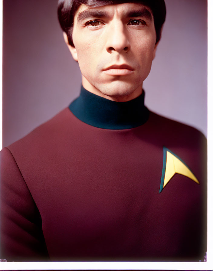 Man in burgundy uniform with futuristic insignia gazing intently