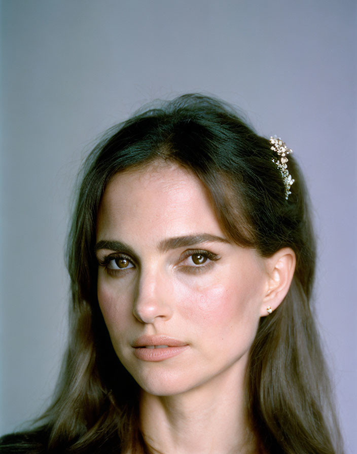 Portrait of woman with dark hair and jeweled hair accessory on blue-grey background