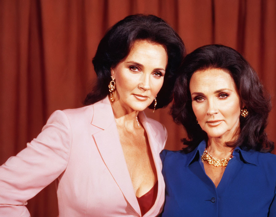 Two women in pink and blue blazers with dark hair and makeup on brown background