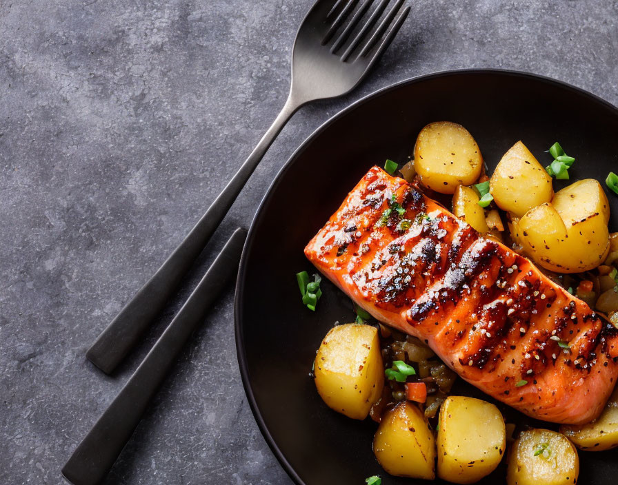 Grilled Salmon Fillet with Golden Potatoes and Herbs on Black Plate