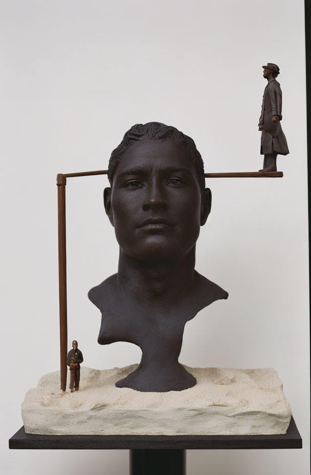 Sculpture of human head with crossbar and miniature figures on plain background