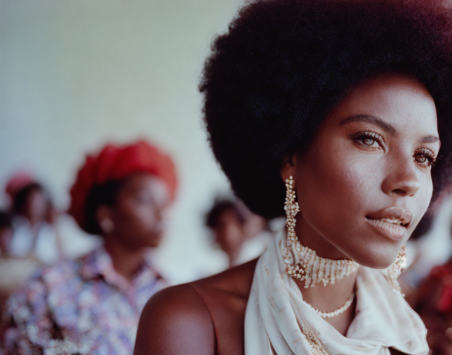 Portrait of a woman with afro and elegant jewelry in focus, surrounded by blurred figures.