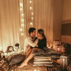 Romantic bedroom with string lights, embracing couple, cushions, and candles