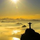 Silhouette of cross on mountain under golden sky with misty mountains.