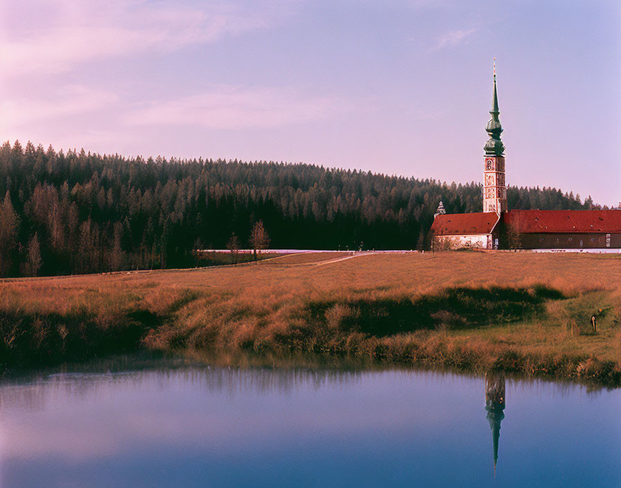 Tranquil church by forest reflected in calm lake at dusk