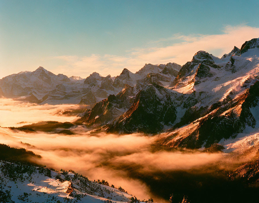 Snowy mountain range at sunset with golden peaks and misty valleys