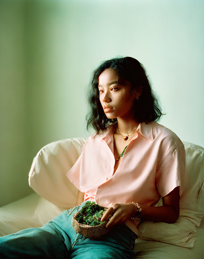 Contemplative woman in pink shirt and denim holding potted plant in soft light