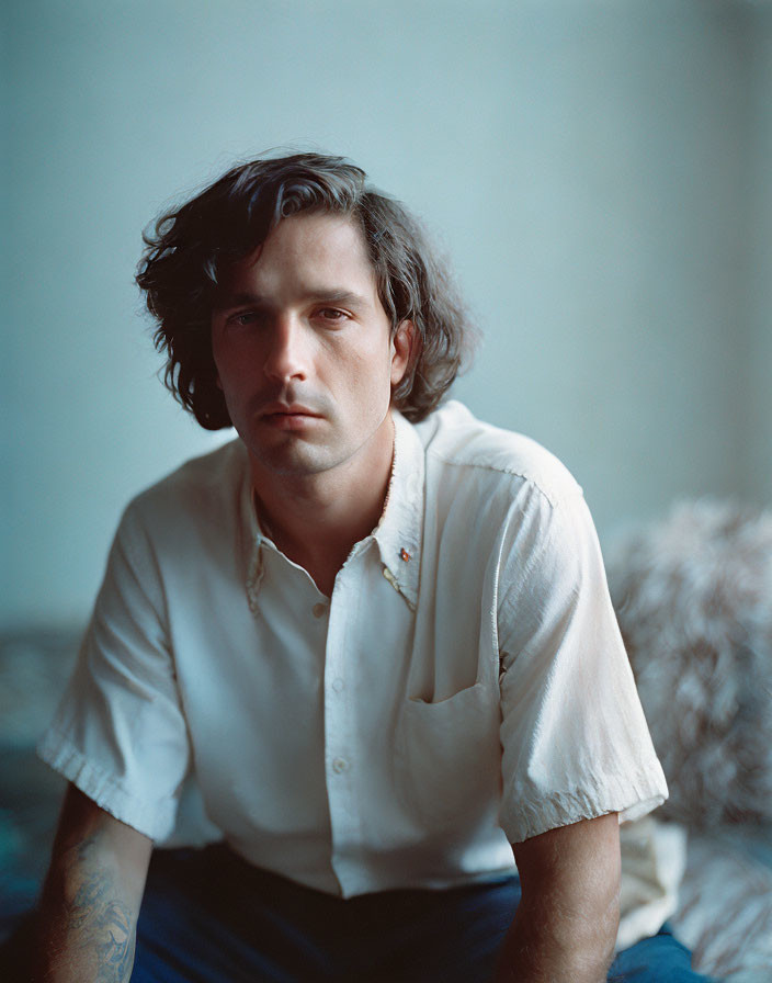 Man with Shoulder-Length Hair and Arm Tattoo Sitting in White Shirt