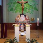 Altar with crucifix, floral decorations, candles, and religious statues on painted cross backdrop.