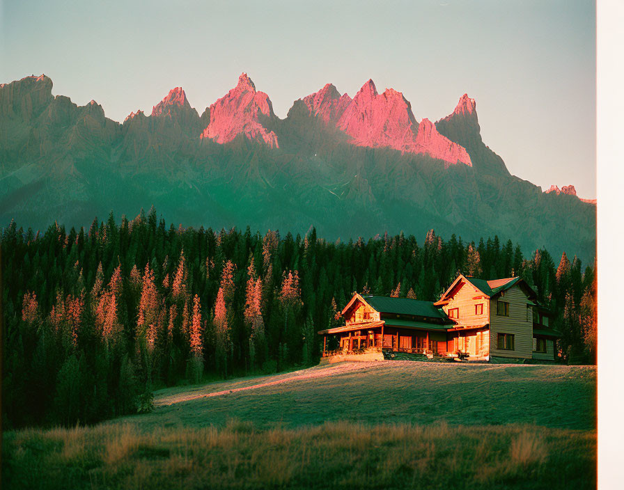 Tranquil sunset landscape with wooden cabin and pink-lit mountains