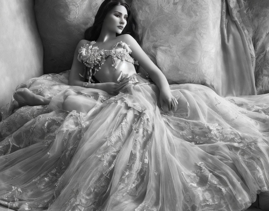 Elegant woman in floral gown reclining on draped fabric in black and white.