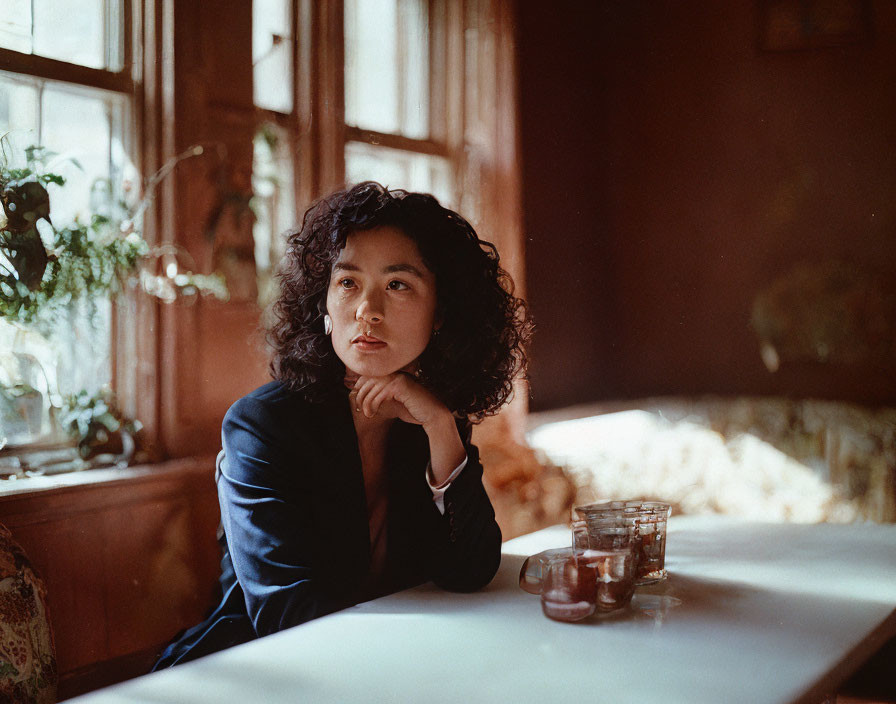 Curly Haired Woman Sitting by Window Lost in Thought