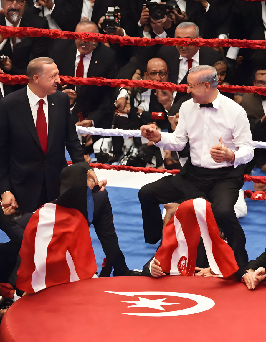Men in formal attire with flag-themed robes in boxing ring with spectators.