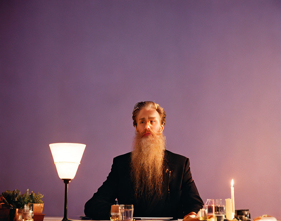 Bearded man in suit at dining table with candles, lamp, and plants