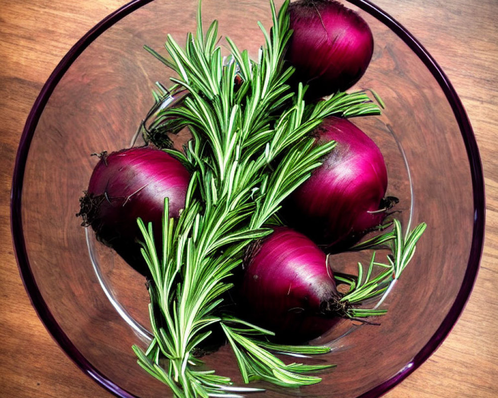 Glass bowl with red onions and rosemary on wooden surface