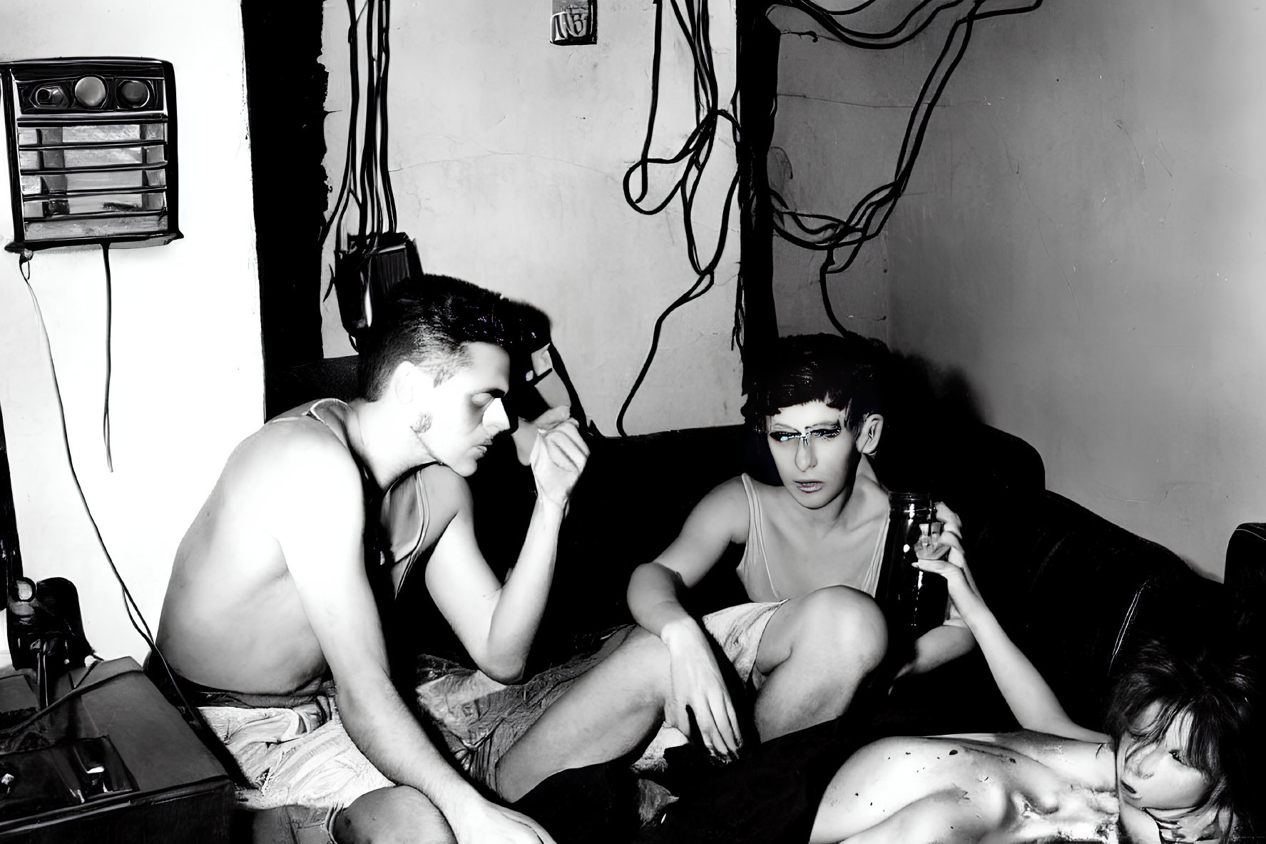Monochrome photo of three people in messy room with wires and cassette player