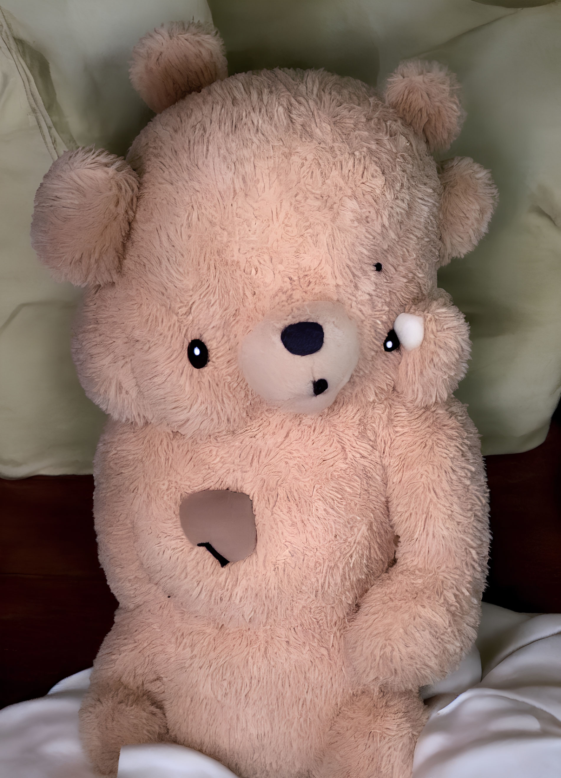 Plush teddy bear with missing eye and heart-shaped hole on chest on green pillow bed