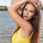 Woman with long wavy hair and blue eyes in yellow outfit by the sea