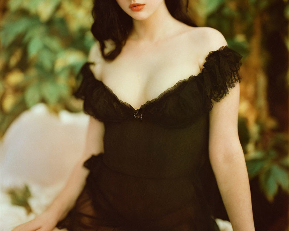 Elegant woman in black off-shoulder dress against soft-focus greenery