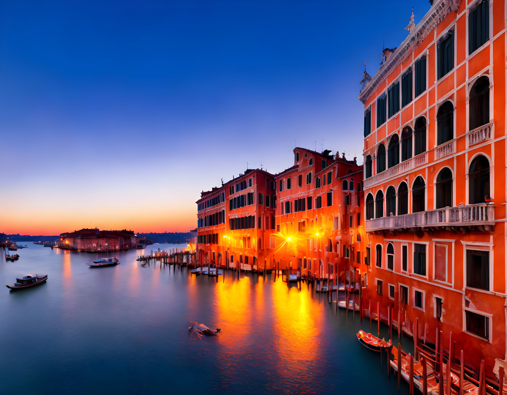 Illuminated Venetian canal at twilight with reflecting buildings and moored boats