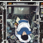 Person lying on glass floor in space station interior with cosmos below