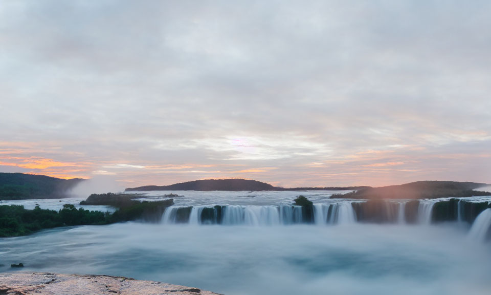 Tranquil waterfall scene with evening sky and distant hills